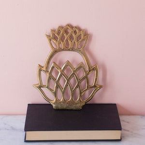 May include: A gold metal bookend in the shape of a stylized pineapple. The bookend is sitting on top of a black book.
