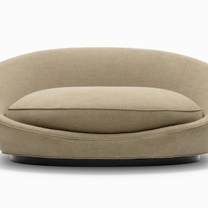 May include: A beige, modern-style sofa with a rounded back and a matching rectangular cushion. The sofa sits on a dark, circular base. The overall design is minimalist and contemporary, suitable for a living room or lounge area.