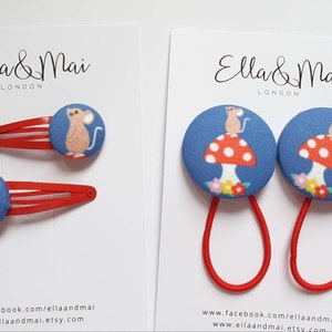May include: Two red hair clips with blue and white fabric buttons featuring a mouse on a mushroom. Two red hair ties with the same blue and white fabric buttons.