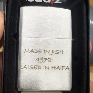 Puede incluir: Un encendedor plateado con el texto "MADE IN JISH 1972 RAISED IN HAIFA" grabado en la parte delantera. El encendedor est&aacute; en una caja negra con el nombre de la marca "oddz" impreso en la tapa. La parte inferior de la caja dice "Made in USA".