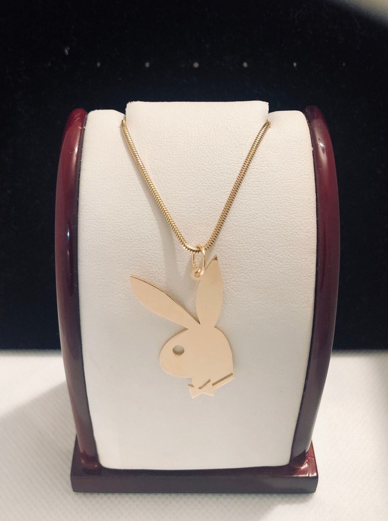 May include: A gold chain necklace with a gold pendant shaped like the Playboy bunny logo.
