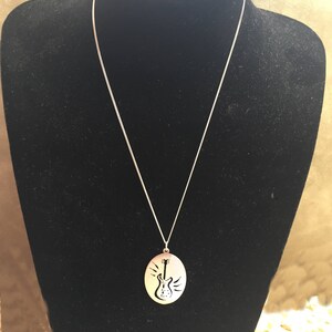 以下が含まれることがあります： 電気ギターのカットアウトデザインが施された楕円形のペンダントが付いたシルバーチェーンネックレスです。