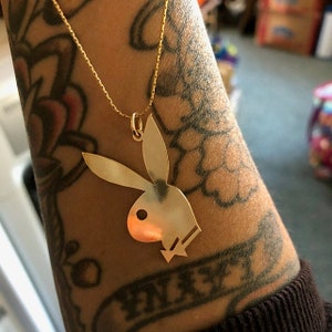 May include: A gold chain necklace with a gold pendant shaped like the Playboy bunny logo.