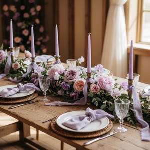 May include: A rustic wooden table set for a special occasion, featuring floral centerpieces with pink and purple roses, lavender candles, and elegant place settings with white plates and crystal glassware.