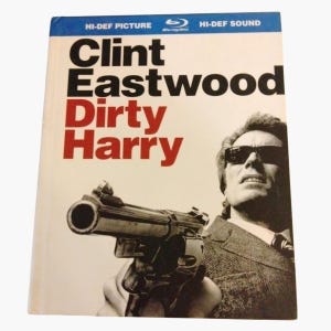 May include: A Blu-ray disc case for the film Dirty Harry featuring Clint Eastwood wearing sunglasses and holding a large revolver. The cover has a white background with black text reading Clint Eastwood and red text reading Dirty Harry.