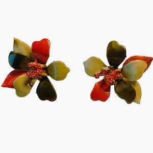 May include: A pair of flower-shaped earrings. Each earring features petals in shades of red, green, and yellow, with a cluster of small red beads at the center. The earrings are set against a white background.
