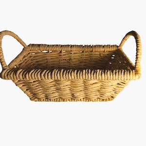 May include: A woven wicker basket with two handles. The basket is light brown and has a rectangular shape.