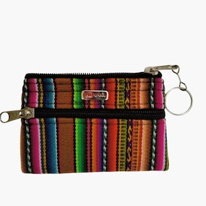 May include: A small, rectangular coin purse with a colorful striped pattern in shades of pink, orange, green, and brown. The purse has a black zipper and a silver-tone metal ring attached. A small metal tag with the word "Oui" is on the front.