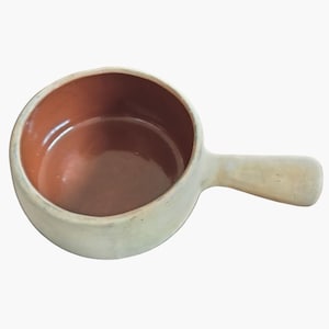 Puede incluir: Un pequeño cuenco de cerámica blanquecina con un asa. El interior del cuenco es de color marrón cálido, contrastando con el exterior. El asa es una continuación del color blanquecino del cuenco. El cuenco está diseñado para cocinar o servir.