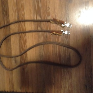May include: Two brown leather reins with silver snap hooks. The reins are lying on a wooden surface.