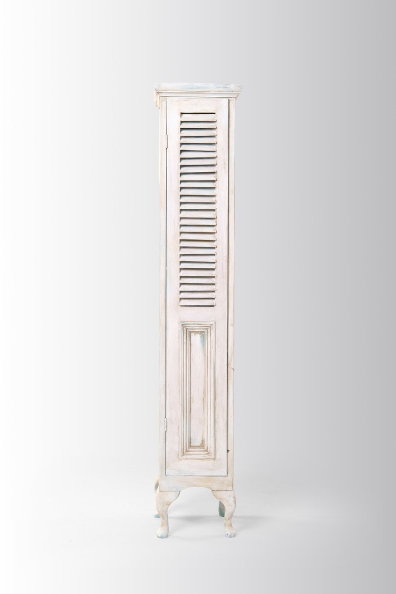 Pu&ograve; includere: Un armadio in legno bianco con una porta a persiane e quattro gambe. L'armadio ha una finitura di vernice invecchiata.