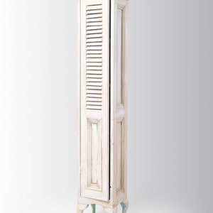 May include: A white wooden cabinet with a shuttered door and decorative legs. The cabinet has a distressed paint finish and is a tall, narrow design.