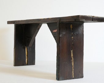 Può includere: Una panca in legno rustica con una finitura marrone scuro e dettagli dorati. La panca ha un design semplice con un piano rettangolare e due gambe su ogni lato. Le gambe sono realizzate con spessi assi di legno che sono uniti nella parte superiore.
