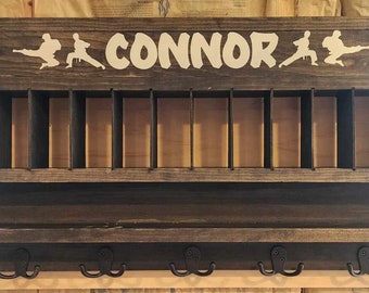 May include: A dark stained wooden wall organizer with multiple compartments and hooks. The top features the name "CONNOR" in white lettering, along with karate figures. The organizer has a shelf and five metal hooks.
