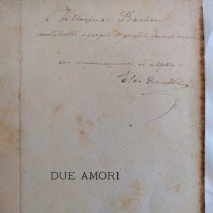 Puede incluir: Una página de libro antiguo con escritura manuscrita y el título "DUE AMORI" impreso en negro. La página está envejecida, con manchas marrones y un borde desgastado, lo que sugiere que es una antigüedad. La escritura parece ser en italiano.