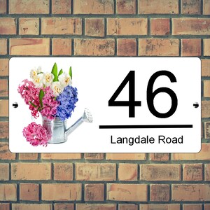 May include: White sign with black text and a floral design. The sign reads "46 Langdale Road". The floral design features pink, white, and blue flowers in a silver watering can.