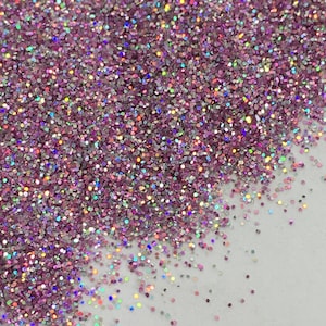 May include: Pink iridescent glitter with a holographic finish. The glitter is scattered on a white surface.