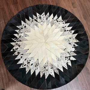 Könnte beinhalten: Runder Kuhfellteppich in Schwarz und Weiß mit einem Sternmuster. Der Teppich hat einen Durchmesser von etwa 1,2 Metern.