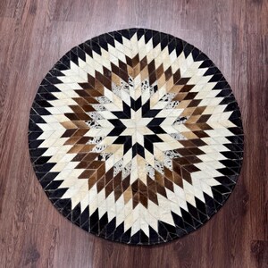 Pode incluir: Tapete redondo com um design geom&eacute;trico de estrela. O tapete apresenta um padr&atilde;o de losangos em tons de preto, castanho, creme e branco. O tapete &eacute; feito de um material natural, provavelmente pele ou couro.
