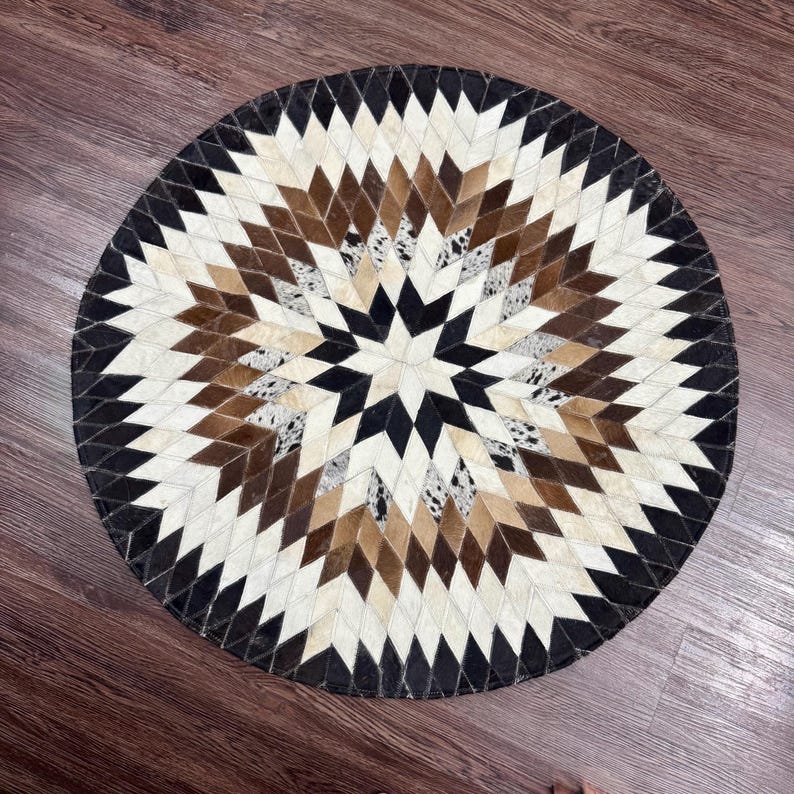 Pode incluir: Tapete redondo com um padr&atilde;o geom&eacute;trico de estrela. O tapete apresenta formas de diamante em pele de vaca preta, branca, castanha e bege. A borda externa &eacute; uma borda preta s&oacute;lida. Este tapete decorativo &eacute; adequado para uma sala de estar ou quarto.