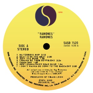 May include: A yellow vinyl record with a black and white yin yang symbol in the center. The record is labeled "Side A Stereo" and features the song titles "Blitzkrieg Bop", "Beat Is On The Brat", "Judy Is A Punk", "I Wanna Be Your Boyfriend", "Chain Saw", "Now I Wanna Sniff Some Glue", and "I Don't Wanna Go Down To The Basement". The record is by the band "Ramones" and is titled "Ramones". The record label is "Sire Records Inc."