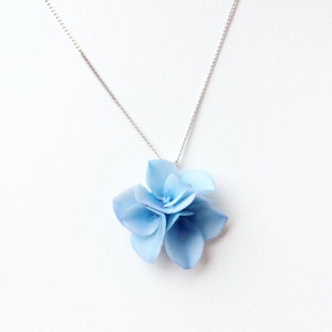 以下が含まれることがあります： 薄い銀色のチェーンネックレスに、薄い青色の花の形をしたペンダントがついたネックレス。花は複数の花びらの層でできており、立体的な効果を生み出しています。