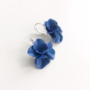 May include: A pair of blue flower earrings with silver hooks. The flowers are made of fabric and have a layered, three-dimensional look.