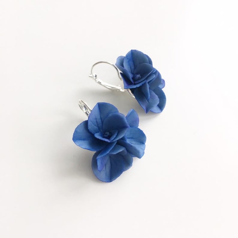 May include: A pair of blue flower earrings with silver hooks. The flowers are made of fabric and have a layered, three-dimensional look.