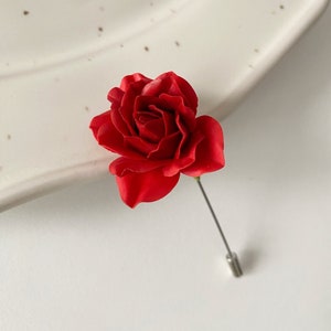 May include: A red rose lapel pin with a silver pin.