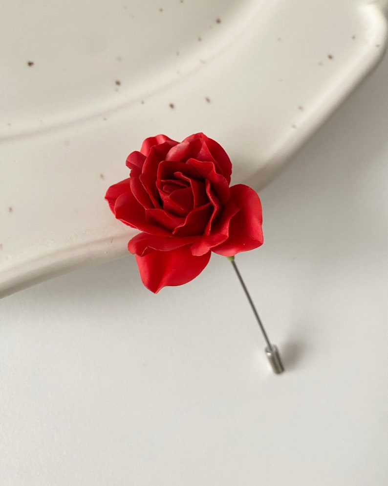 May include: A red rose lapel pin with a silver pin.