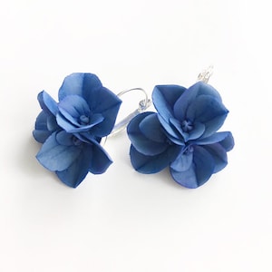 May include: A pair of blue flower earrings with silver hoops. The flowers are made of fabric and have a layered look.