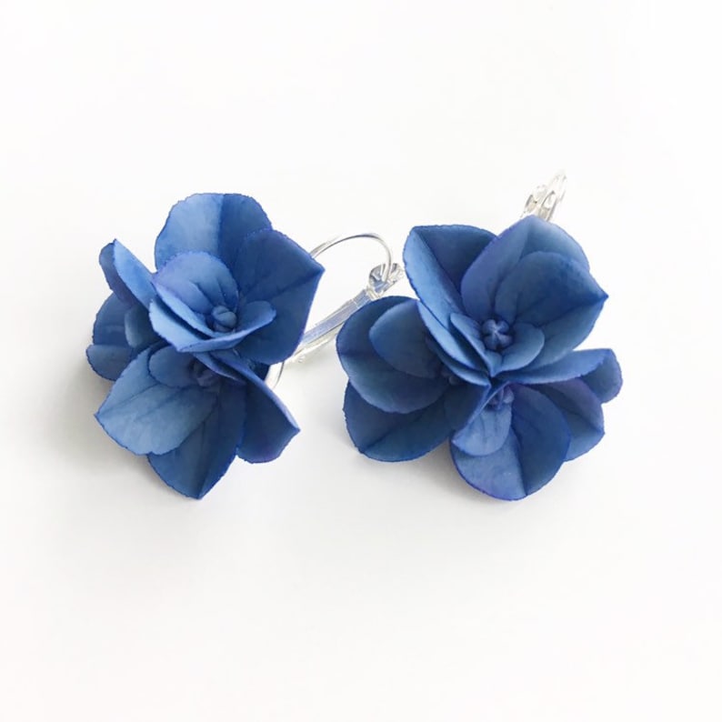 May include: A pair of blue flower earrings with silver hoops. The flowers are made of fabric and have a layered look.