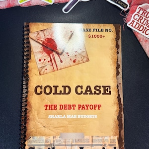 May include: A spiral-bound notebook with a tan, aged-paper cover featuring the text COLD CASE, THE DEBT PAYOFF, SHARLA MAE BUDGETS, and Strikes Again! The cover displays a graphic of a blood-stained envelope and a newspaper-style bottom border.