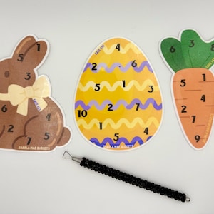 May include: An Easter-themed set featuring a brown bunny, a yellow egg, and an orange carrot, each with numbers. A black stylus is also present. The bunny has a bow, and the egg and carrot have wavy patterns.