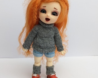 May include: A small doll with long, curly orange hair wearing a gray sweater, denim shorts, gray socks, and red shoes.