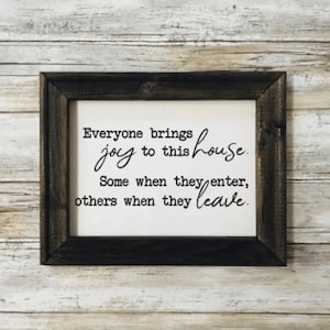 May include: A framed sign with a white background and black text that reads "Everyone brings joy to this house. Some when they enter, others when they leave."
