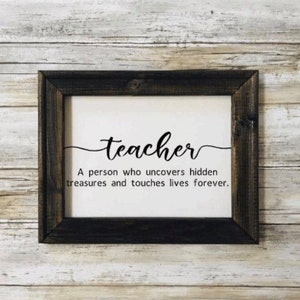 May include: A framed sign with the word "teacher" in cursive script. The sign reads "A person who uncovers hidden treasures and touches lives forever."