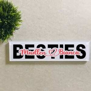 May include: White plaque with black text that reads "Bestes Madlen & Bianca" with a red heart between the names.