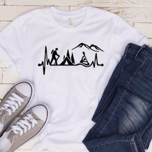 May include: White t-shirt with a black graphic of a heartbeat with a hiker, a tent, a mountain, and a kayaker. The graphic is centered on the shirt.