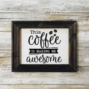 May include: A black framed sign with white background and black text that reads "This coffee is making me awesome" with three coffee beans above the word "coffee".