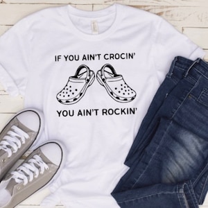 May include: White t-shirt with black text that reads "If you ain't crocin' you ain't rockin'" and a graphic of two black and white Crocs.