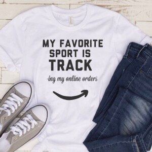May include: White t-shirt with black text that reads "My favorite sport is track -ing my online orders" with an Amazon logo underneath.