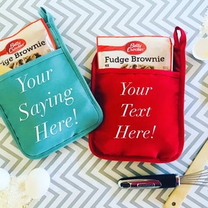 May include: Two red and blue oven mitts with pockets for holding a box of brownie mix. The mitts are personalized with the text "Your Saying Here!" and "Your Text Here!"