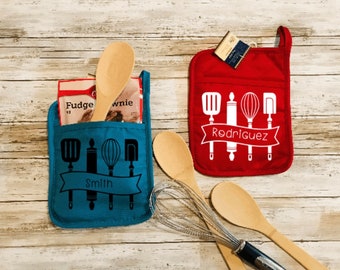 May include: Two personalized oven mitts with a pocket. The blue mitt has a black design of kitchen utensils and the text "Smith". The red mitt has a white design of kitchen utensils and the text "Rodriguez".