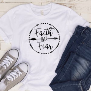 May include: White t-shirt with a black graphic that says "Faith over Fear" with arrows and dots around the text.