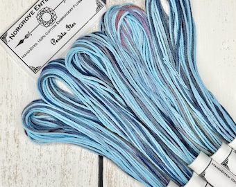 May include: A set of eight skeins of hand-dyed cotton embroidery floss in shades of blue. The floss is wound on white spools with black labels that read "Norgrove Enterprises" and "Hand-Dyed 100% Cotton Embroidery Floss (8m)".