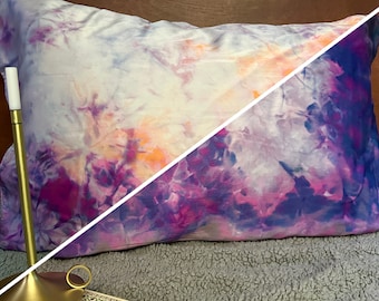 Puede incluir: Una funda de almohada de color morado y naranja con un diseño tie-dye sobre un fondo blanco. La funda de almohada está hecha de un tejido suave y sedoso y es perfecta para añadir un toque de color a tu dormitorio.