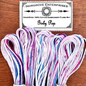 Pode incluir: Fio de bordar de algodão tingido à mão em tons de branco, rosa, azul e roxo. A etiqueta diz "Girly Pop" e "NORGROVE ENTERPRISES". Cada meada tem 8 metros. Ideal para bordar e trabalhos manuais.