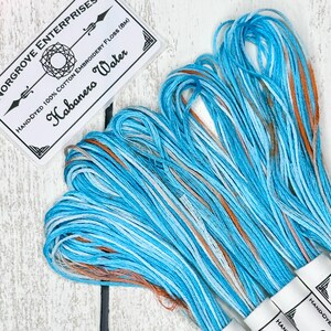 May include: A skein of hand-dyed cotton embroidery floss in a blue, white, and orange color scheme. The floss is labeled "Habanero Water" and is 8 meters long.