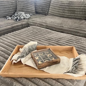 May include: A wooden tray with a gray and white patterned fabric and a wooden tic-tac-toe game with gold pieces.